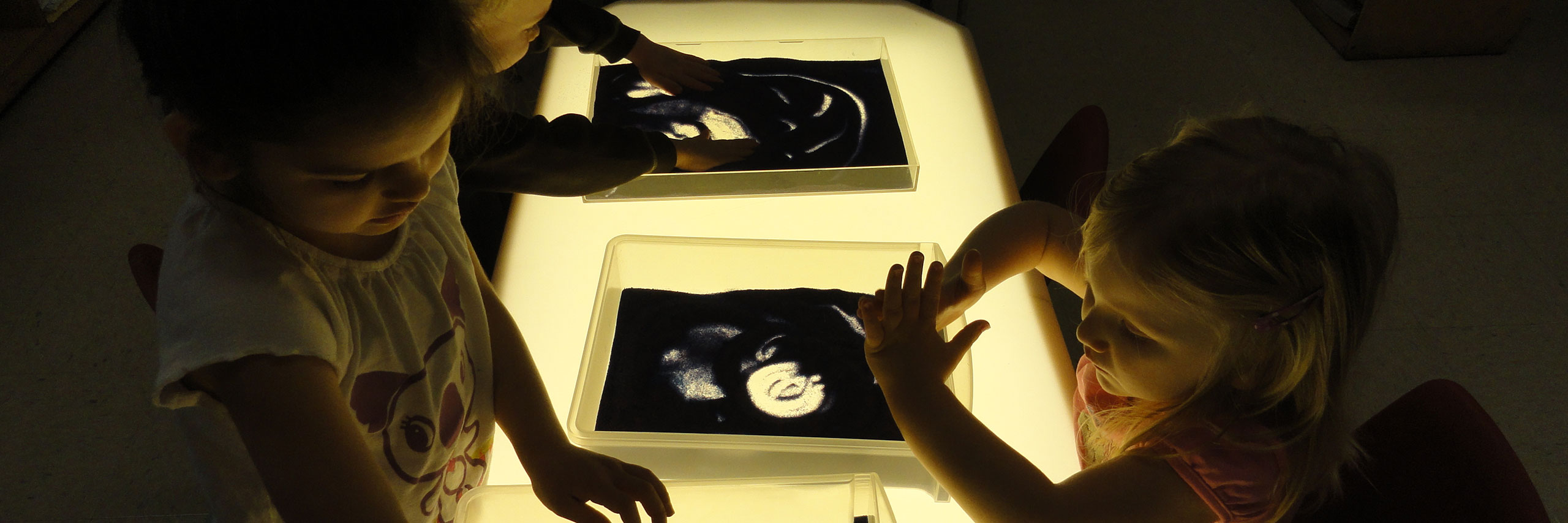 Kids playing with a box of sand on a lighted table.